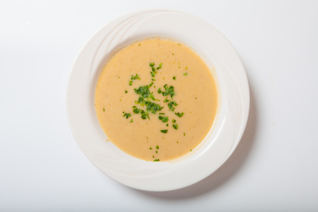 Creamy vegetables soup with fresh herbs in a white bowl. White backgroundの写真素材