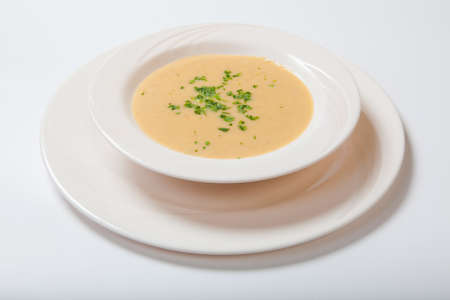 Creamy vegetables soup with fresh herbs in a white bowl. White backgroundの写真素材