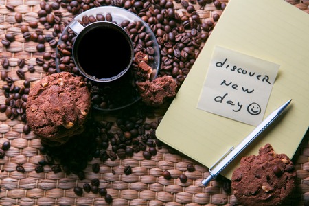 coffee cup and coffee beans on wooden table with cookies and notepad with message on the sticker.の写真素材