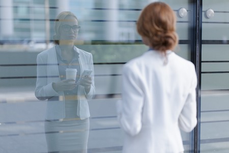 Young beautiful girl looking at her reflection in the window next to business center.の写真素材