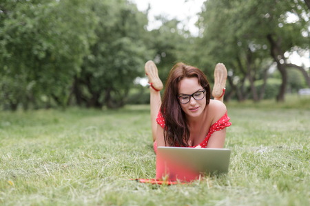 Relaxed beautiful woman lying on the grass and working on laptop.の写真素材