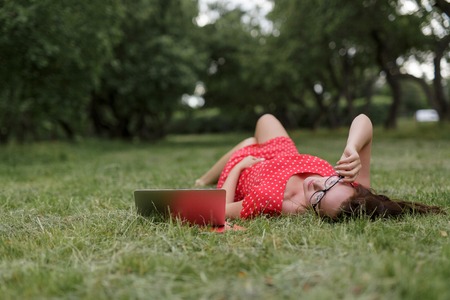 Relaxed beautiful woman lying on the grass and working on laptop.