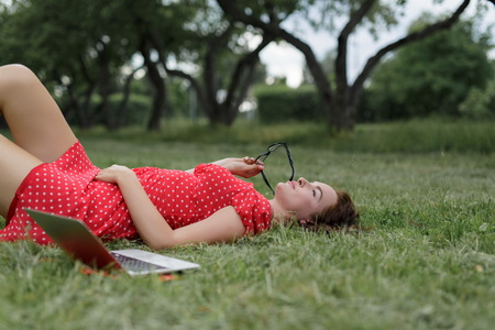 Relaxed beautiful woman lying on the grass next her laptop.