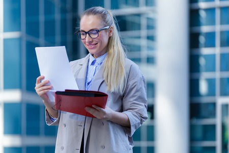 The young woman in gray office dress holds in hand folder with documents. Businesswoman standing next to the business centerの写真素材