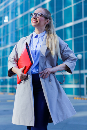 The young woman in gray office dress holds in hand folder with documents. Businesswoman standing next to the business centerの写真素材