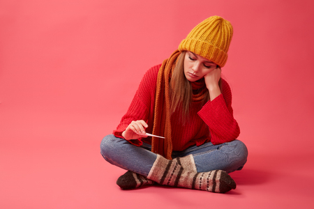 A diseased woman in a yellow hat holds a medical thermometer in her hands. Image on the pink backgroundの写真素材