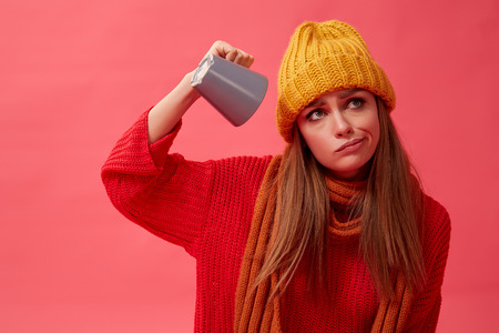 Beautiful woman in warm cozy sweater with cup of hot drink. Red background. Studio