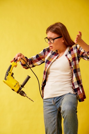 Girl scared holding a drill, standing between the boxes. Yellow backgroundの写真素材