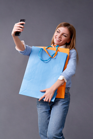 Young woman making a selfie on your smartphone sitting with colored bags for shopping. Studioの写真素材