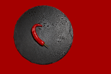 One chili pepper or cayenne pepper on a black slate dish on a red background. Image. Close up.の写真素材