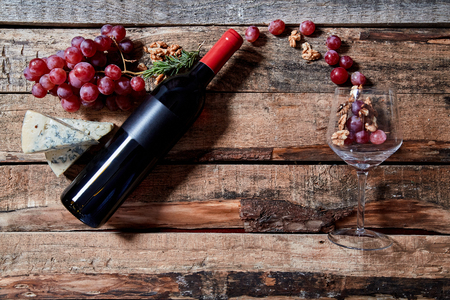 From above layout of grapes and walnuts flying from wine bottle into transparent wineglass on wood backgroundの写真素材