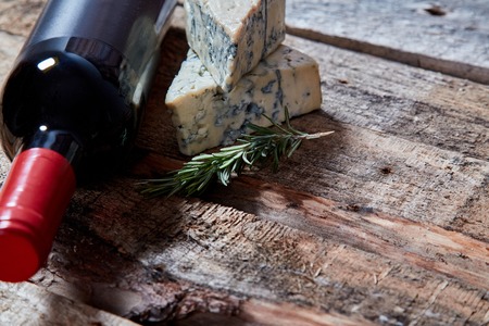 Bottle of red wine on rough wood surface with aromatic blue cheese and bread with walnuts and rosemaryの写真素材