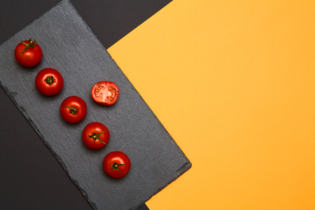 Ripe cherry tomatoes composed on black slate boards on colorful backgroundの写真素材