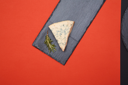 Composition of blue cheese and rosemary on black slate on red backgroundの写真素材