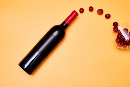 Composition of grapes flying from bottle of wine into shiny wineglass on yellow backgroundの写真素材