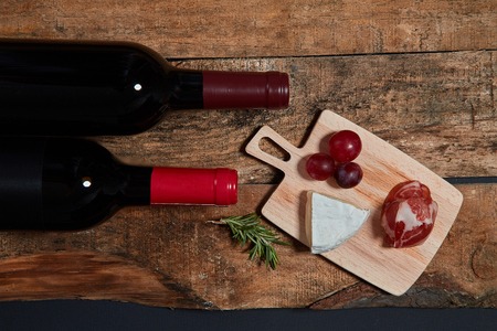 Top view of served snacks on board with twig of rosemary and bottles of red wine on woodの写真素材
