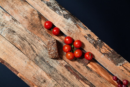Bright red ripe tomatoes on branch covered with water drops composed on wood planksの写真素材
