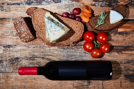 Layout of delicious gourmet snacks with bread and cheese and fruit on wooden planks with bottle of red wine.の写真素材