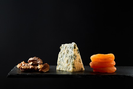 Composition of pieces of walnut and hard cheese and dried apricot on black background.の写真素材