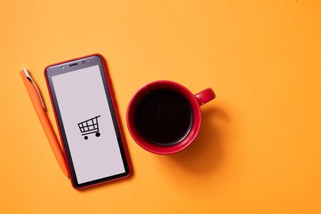 Online shopping and e-commerce. Smartphone and a Cup of coffee on a yellow background.