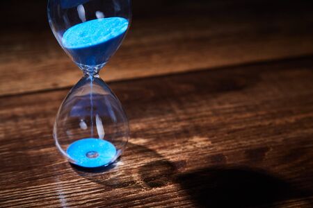 Time passing, deadline, urgency concept. Time management. Blue hourglass on wooden background. Copy...