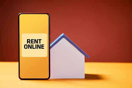 Rent online. Booking property via smartphone app. Reservation accommodation for holiday trip. Planning travelling concept. Miniature house mockup with copy space. Red and yellow backgroundの写真素材