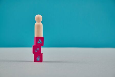 Reach goal and winning. Professional development, leadership. Wooden human figure on cubes with growth, teamwork signsの写真素材