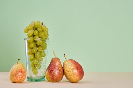 Bunch of grapes in glass. Juicy pears on beige table. Diet. Summer fruits concept. Copy space on green backgroundの写真素材