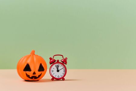 Autumn holiday. Halloween concept. Scary orange pumpkin and red clock. Copy space for text. Isolated on green backdropの写真素材