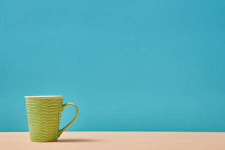 Utensils. Teacup. Tableware concept. Green cup with wavy decor. Vessel for drink. Empty mug. Blue backdrop. Copy spaceの写真素材