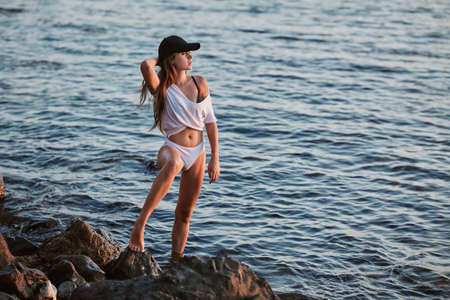 Woman posing on coastline in cap. Relax and contemplation idea. Calm sea and nature landscape....