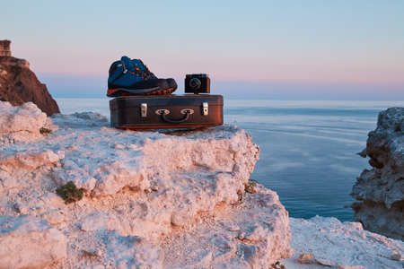 Old suitcase with boots and photocamera on top. Travel desire or Summer season. Cute sunset and...