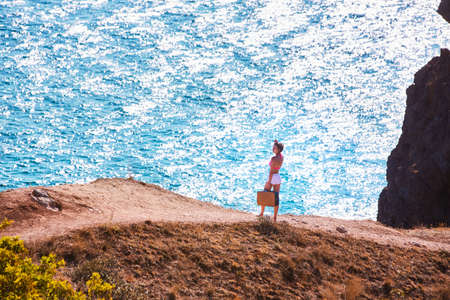 Summer time and tourism. Woman on mountain road with vintage suitcase. Crystal water. Virgin nature. Beach vacationの写真素材