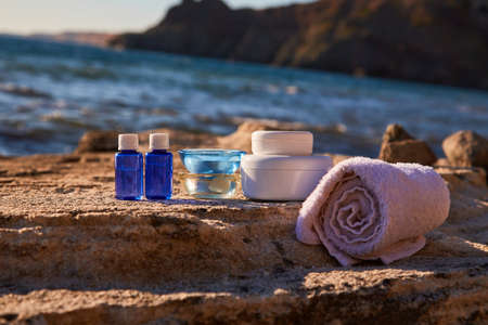 Spa treatment and relax near sea. Bottles with aroma oils and glass candles on rock. Towel and containers with cream.の写真素材