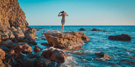 Female posing in trendy hat. Mountain and seaview. Rocky coastline and beach vacation concept....