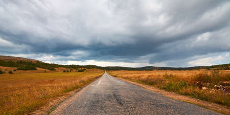 Nature landscape and dark stormy sky. New way and adventure trip. Long road ahead. Travel time concept. Copy spaceの写真素材