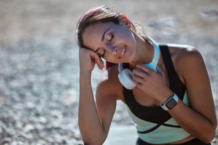 Tired lady rest on beach with headset on neck. Exhausted workout outdoors. Contemplation nature and time alone conceptの写真素材