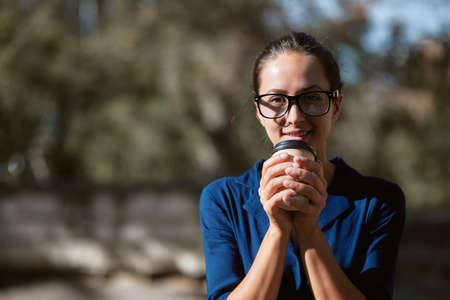 Pretty woman warming up with cup of coffee. Lady in glasses in park. Take break and leisure time...