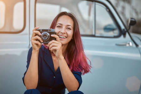 New emotion and travel time concept. Beautiful female taking picture on street with photocamera. Blue car on background.の写真素材
