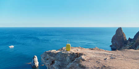 Vacation time freedom and summer time concept. Seagull and yellow suitcase on mountain top. Yacht floating on oceanの写真素材