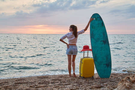Woman on holiday, surfboard and suitcase. Sunset over ocean, sense of adventure and relaxation time concept. Copy spaceの写真素材
