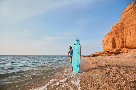 Beach, adventure time and summer holiday concept. Cute woman with surfboard on nature landscape...