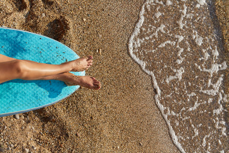 Holiday trip, summer time and time to relax idea, copy space. Womans legs getting tanned on sun. Wet sand on coastline.の写真素材
