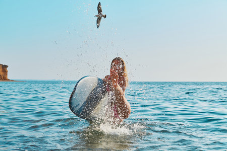 Woman having fun in ocean, spray with water. Bird flying in blue sky. Holiday trip, surfing sport and summer time ideaの写真素材