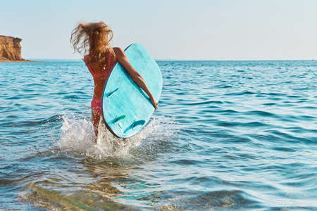 Girl running in sea water with surfboard. Lady learn surfing on vacation. Surfing sport, summer time...