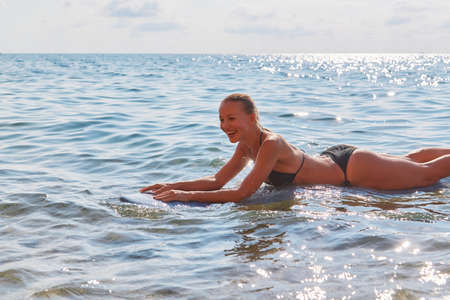 Happy lady floating on surfboard in ocean. Wavy sea on summer day. Surf sport, adventure trip and beach day conceptの写真素材