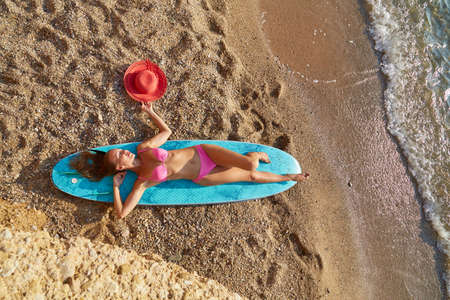 Idea of holiday trip, relax, desire of adventure. Lady sunbath on surfboard, hot sunny weather. Fresh sea air and chill.の写真素材