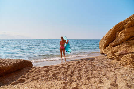 Girl in swimsuit ready to surf in sea. Hot day on beach and ocean view. Idea of summer, relax and desire of adventureの写真素材