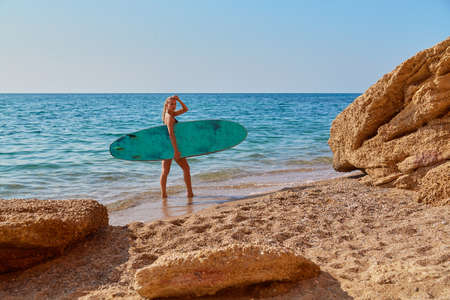 Girl posing with surfboard on coastline. Hot summer day on beach. Summer time, surf sport and vacation idea, copy spaceの写真素材