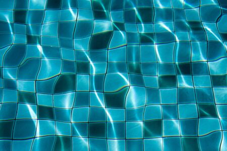 Sun reflection on the blue clear water ripples of swimming pool with mosaic bottomの写真素材